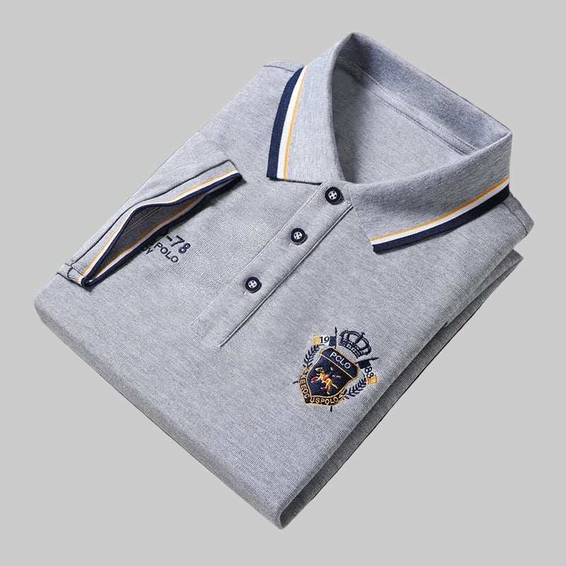 Folded gray polo shirt with brand logo on a dark surface, next to a watch.